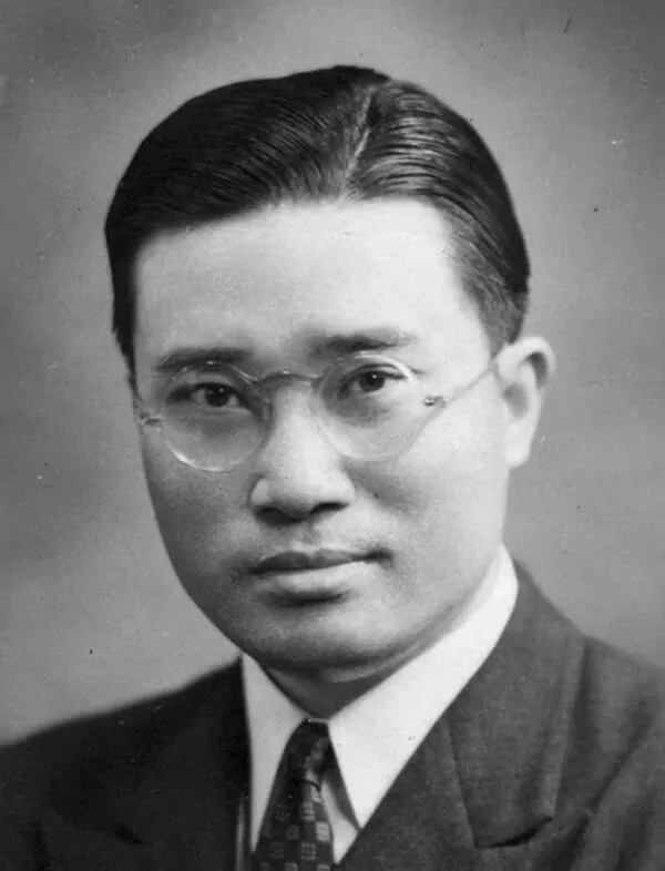 戴圆框眼镜、穿深色西装打领带的年轻男子面部特写,梳背头,表情严肃,柔光影棚背景。