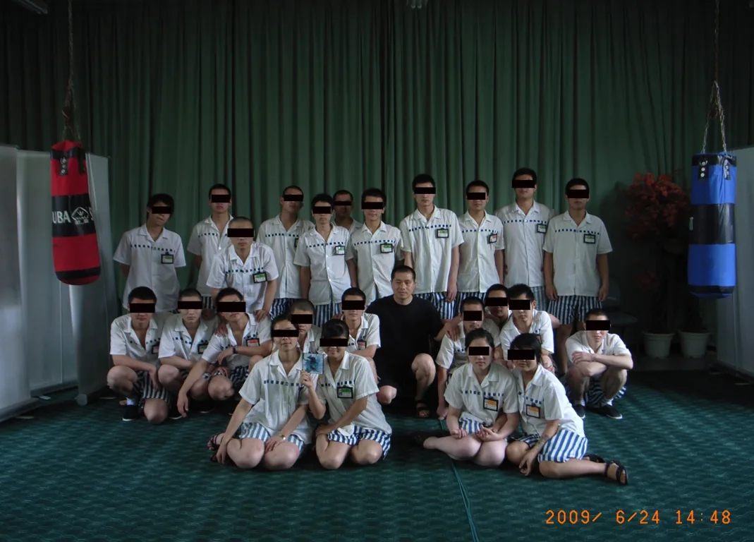 少年犯与艺术家李牧的集体合影:约二十人分两排站坐,李牧居中,前排一女孩手持一张CD,所有少年脸部打码。