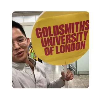 彬华在地铁站内自拍留影,手举黄色标牌,上面写着英文「GOLDSMITHS UNIVERSITY OF LONDON」。