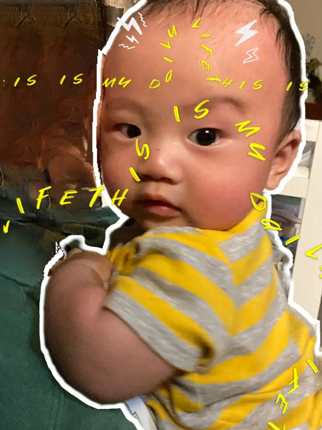经贴纸特效处理的婴儿照片,孩子身穿黄灰条纹上衣,头部周围环绕黄色手写字“this is my life”和白色闪电贴纸装饰。