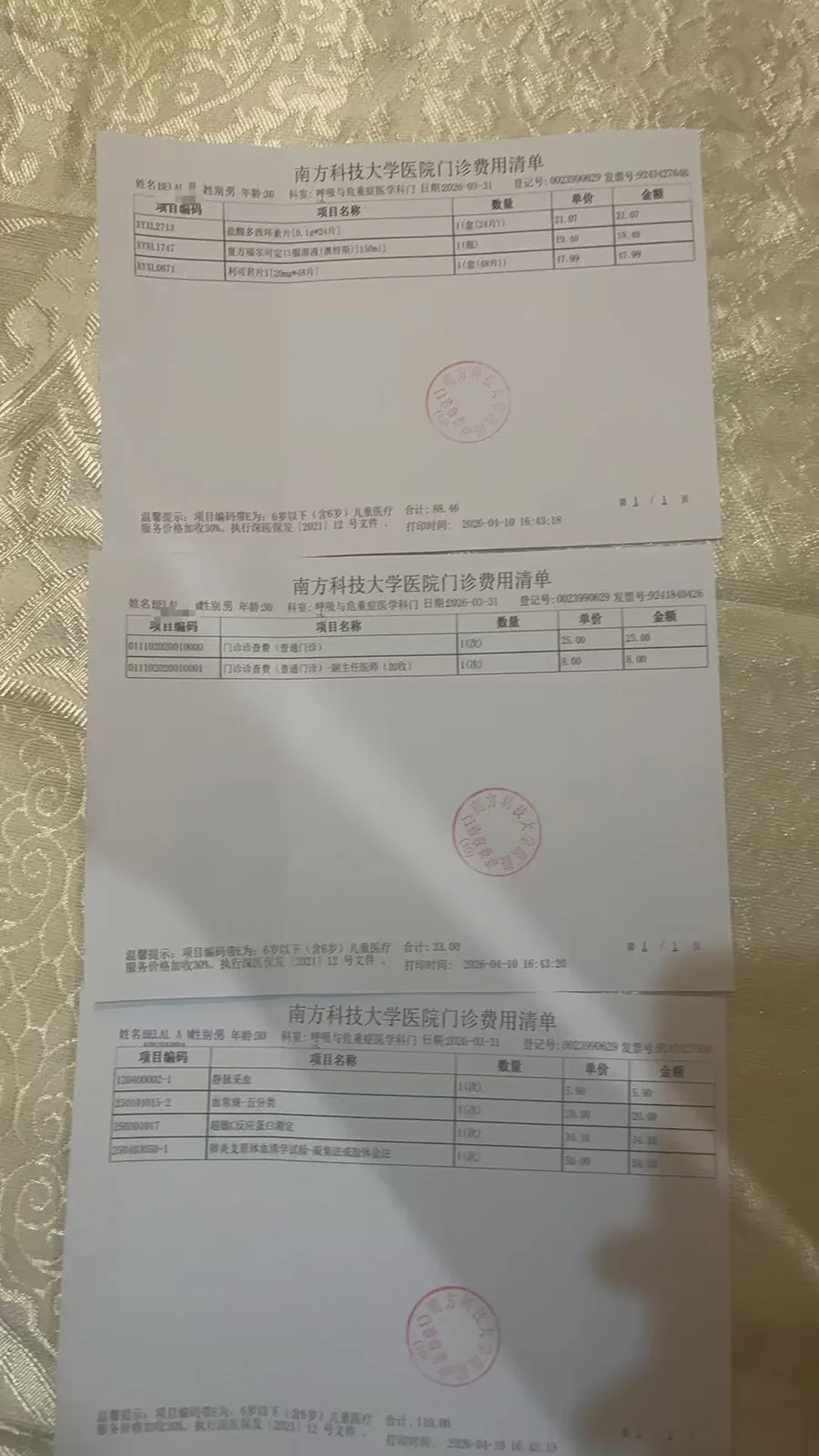 三张南方科技大学医院门诊费用清单叠放在织物上,分别列出药费、检查费等收费项目及金额,均盖有医院印章。