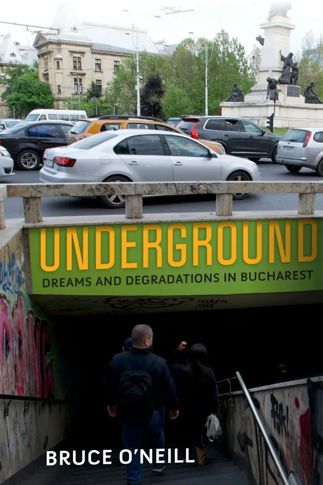 书封《Underground: Dreams and Degradations in Bucharest》,作者 Bruce O'Neill;街景照片,上方车流穿行的马路与身后欧式建筑,两人背影正走下涂满涂鸦的地下通道台阶,入口处绿色招牌写着书名。