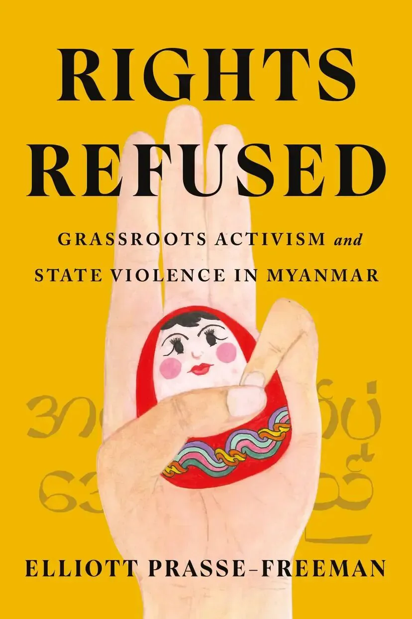 书封《Rights Refused: Grassroots Activism and State Violence in Myanmar》,作者 Elliott Prasse-Freeman;黄色背景上一只手掌张开,掌心画着一枚圆形人偶图案,人偶手中缠绕彩色绳结,背景隐约印有缅文字符。