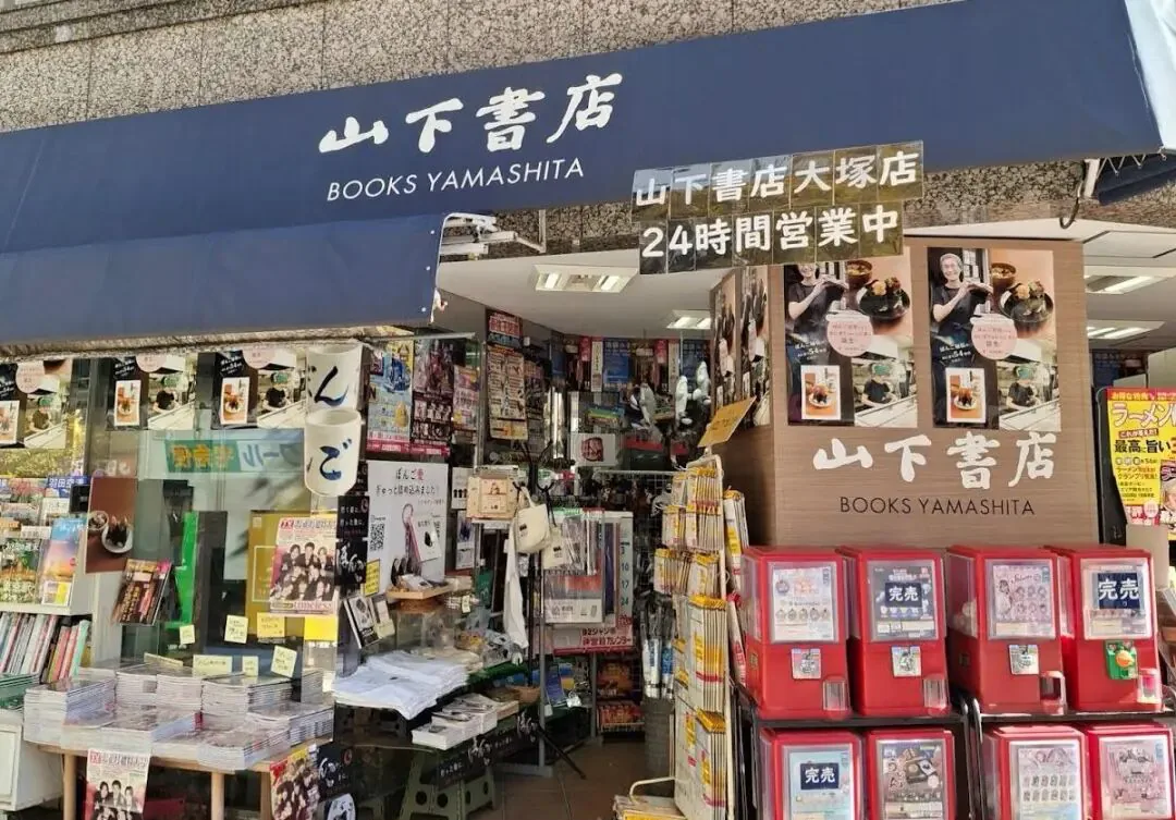 东京一家名为“山下書店”(BOOKS YAMASHITA)的24小时营业书店门面,门口摆满杂志书刊,旁边放着多台红色扭蛋机。