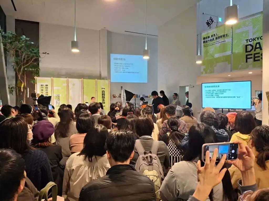拥挤的会场内座无虚席,不少观众站立听讲并举起手机拍照,讲台旁投影着写满文字的演讲提纲,墙上挂着绿色“故事节”主视觉海报。