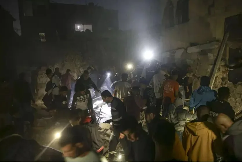 夜间场景,一大群人手持手电筒和手机灯光,在倒塌建筑的瓦砾堆中搜寻,周围是漆黑的废墟和残垣。