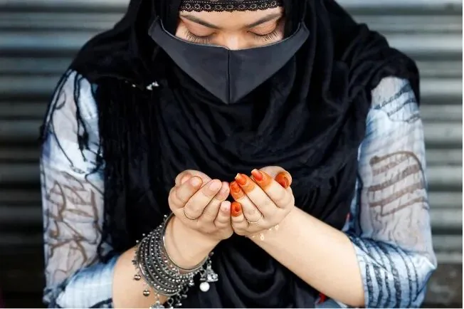 特写镜头下,一名戴黑色面纱的妇女双手合十做祈祷手势,手腕戴银色手镯,指甲染成橙色。