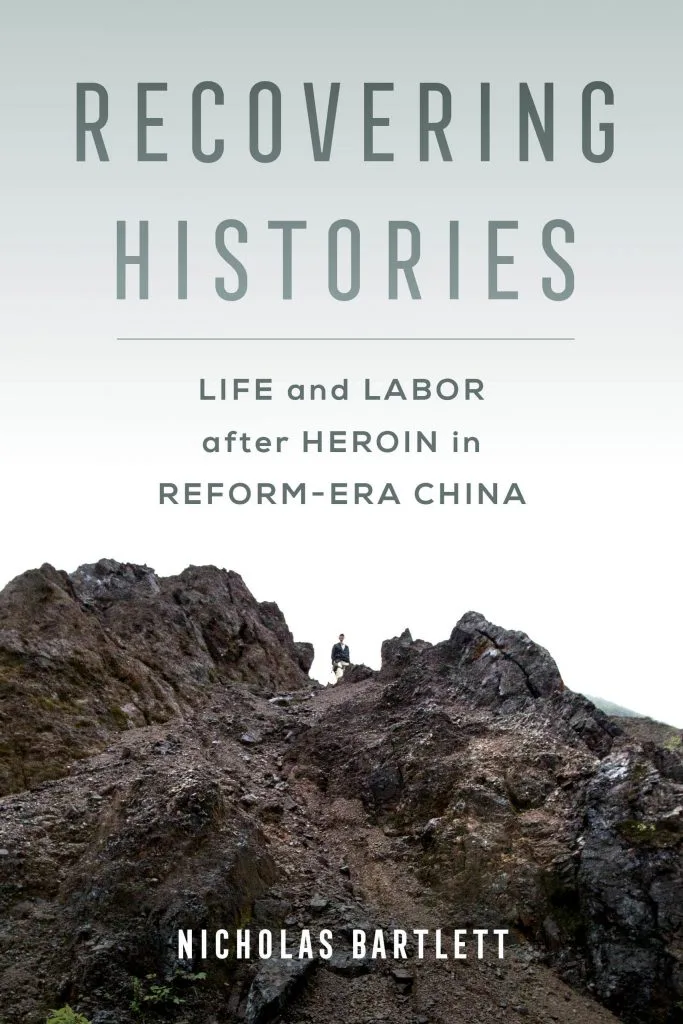 书封,灰绿色调,一人站在嶙峋山脊小径上,书名《Recovering Histories: Life and Labor after Heroin in Reform-Era China》,作者Nicholas Bartlett。
