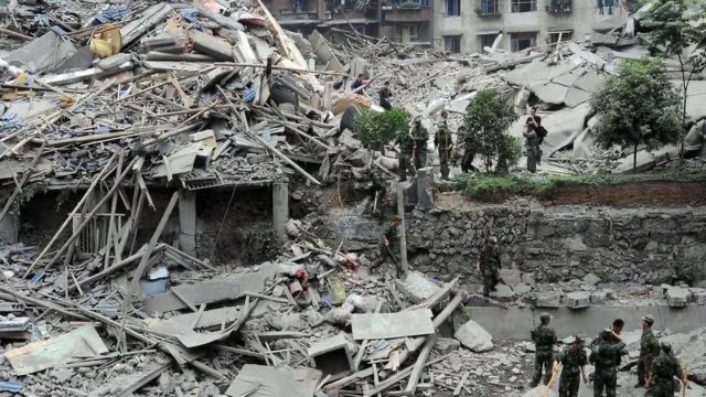 汶川地震后倒塌的多层建筑化为一片废墟,多名迷彩军装士兵在瓦砾间搜救。