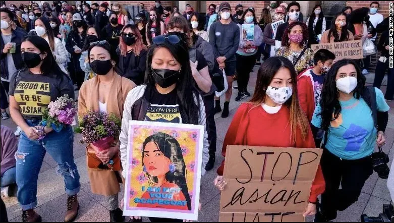 一群戴口罩的亚裔女性举著「STOP ASIAN HATE」和「我不是你的替罪羊」标语牌参加游行,有人手捧鲜花