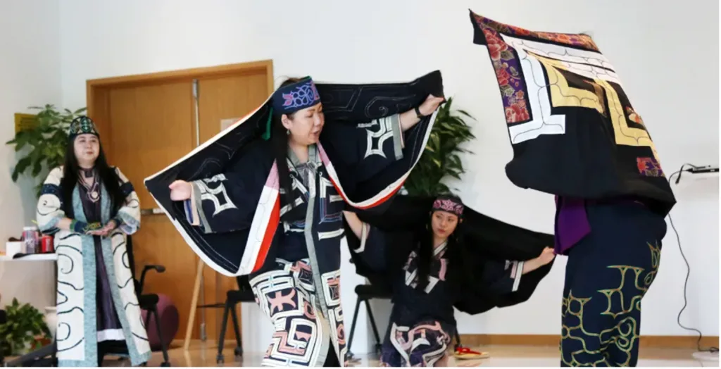 多位身着黑底彩色几何纹样传统长袍、佩戴头巾的表演者围站跳舞,几人张开双臂展开宽大袖摆,动作富有仪式感。