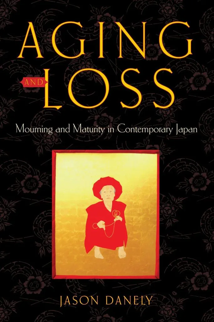 黑底印花封面,中央金色画框里是一位披红衣、戴红帽、蹲坐的老年女性手持念珠,上方印书名《Aging and Loss》与作者 Jason Danely。