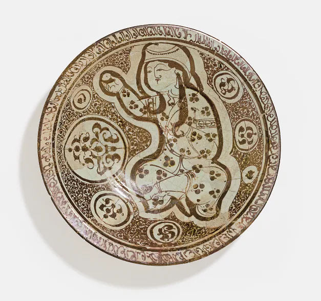 光泽釉圆碗,赭金色纹样:一人物坐姿,一手高举一枚圆形果实,周围饰以圆形花卉纹章和阿拉伯文题字边饰。