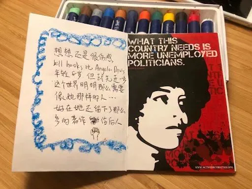 左页蓝色蜡笔描边,手写“想想还是很伤感,bell hooks比Angela Davis年轻5岁,但却无法弥补这个世界明明那么需要像她那样的人……好在她还留下了那么多的著作嘉惠后人”;右页是黑红两色政治海报,绘有爆炸头女性侧面剪影,印着“WHAT THIS COUNTRY NEEDS IS MORE UNEMPLOYED POLITICIANS.”