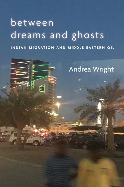 《梦想与幽灵之间》(Between Dreams and Ghosts: Indian Migration and Middle Eastern Oil)封面,作者安德烈娅·赖特(Andrea Wright)。夜色中的城市街景照片,霓虹灯装饰的高楼、棕榈树剪影和停车场,前景有两个模糊的行人身影。
