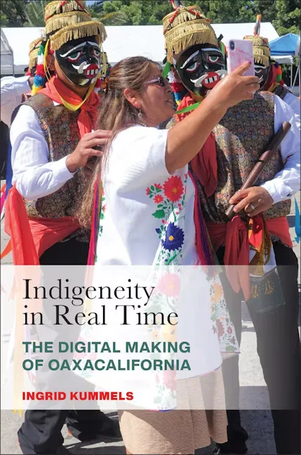 封面书名Indigeneity in Real Time:The Digital Making of Oaxacalifornia,作者Ingrid Kummels;一名穿刺绣上衣的女性举手机自拍,身旁两名男子头戴传统面具和羽饰服装。