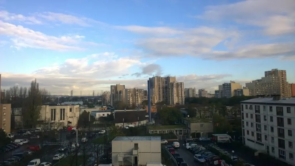 俯瞰视角下的城区全景,多栋高层住宅楼分布在树木和低矮建筑之间,天空多云。