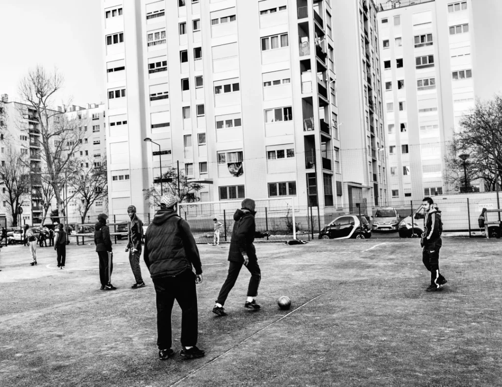 黑白照片:一群男孩在高层住宅楼下的球场上踢足球。