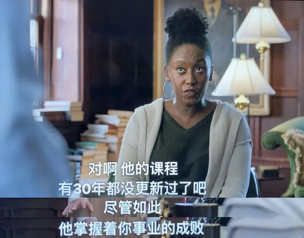 美剧《英文系主任》剧照:一位黑人女性在满是书籍的办公室里说话,字幕写着“对啊,他的课程有30年都没更新过了吧,尽管如此他掌握着你事业的成败”。