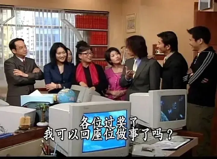 职场剧照配字幕:一群同事围站在办公桌前,中间男子面对众人说话,字幕写着'各位过奖了,我可以回座位做事了吗?'