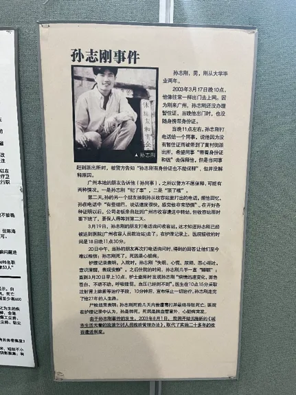 展板题为“孙志刚事件”,左上角为孙志刚坐姿照片,右侧长文讲述他2003年在广州因未携带暂住证被收容后死亡的经过,具体细节文字较小看不清。