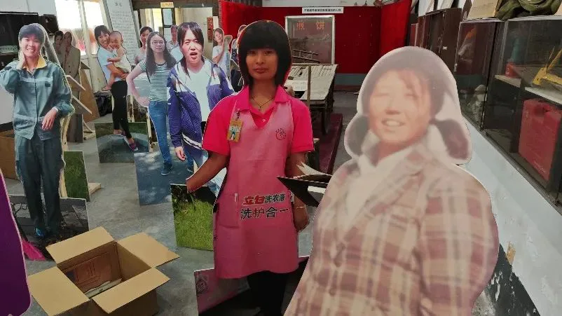 展厅内并排陈列着多个真人大小的女工人形立牌,分别穿着围裙、工装等不同服饰,旁边放着打包用的纸箱。
