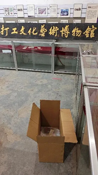 展厅内玻璃展柜已被清空,墙上悬挂“打工文化艺术博物馆”木牌,地面放着一个打包用的纸箱。