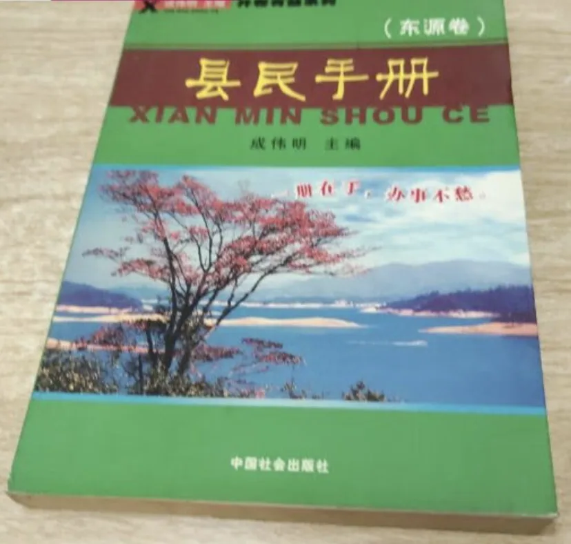 封面绿色底,中间嵌一张湖泊与红叶树的风景照,照片上印有红字标语,书名旁标注拼音“XIAN MIN SHOU CE”。