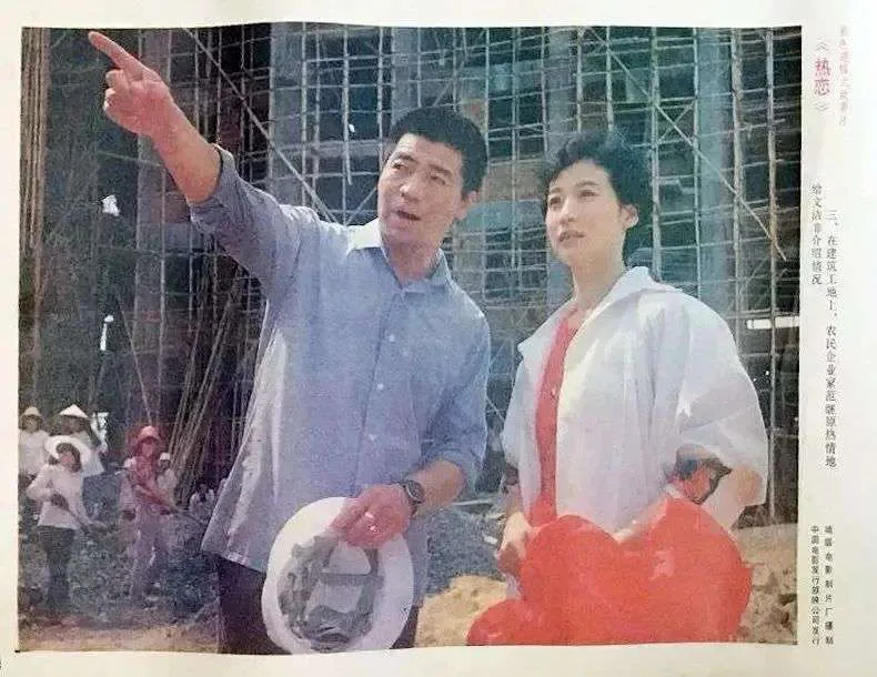剧照:一名男子抬手指向远方,身旁女子随他望去,两人身后是脚手架林立的建筑工地,工人在下方劳作。